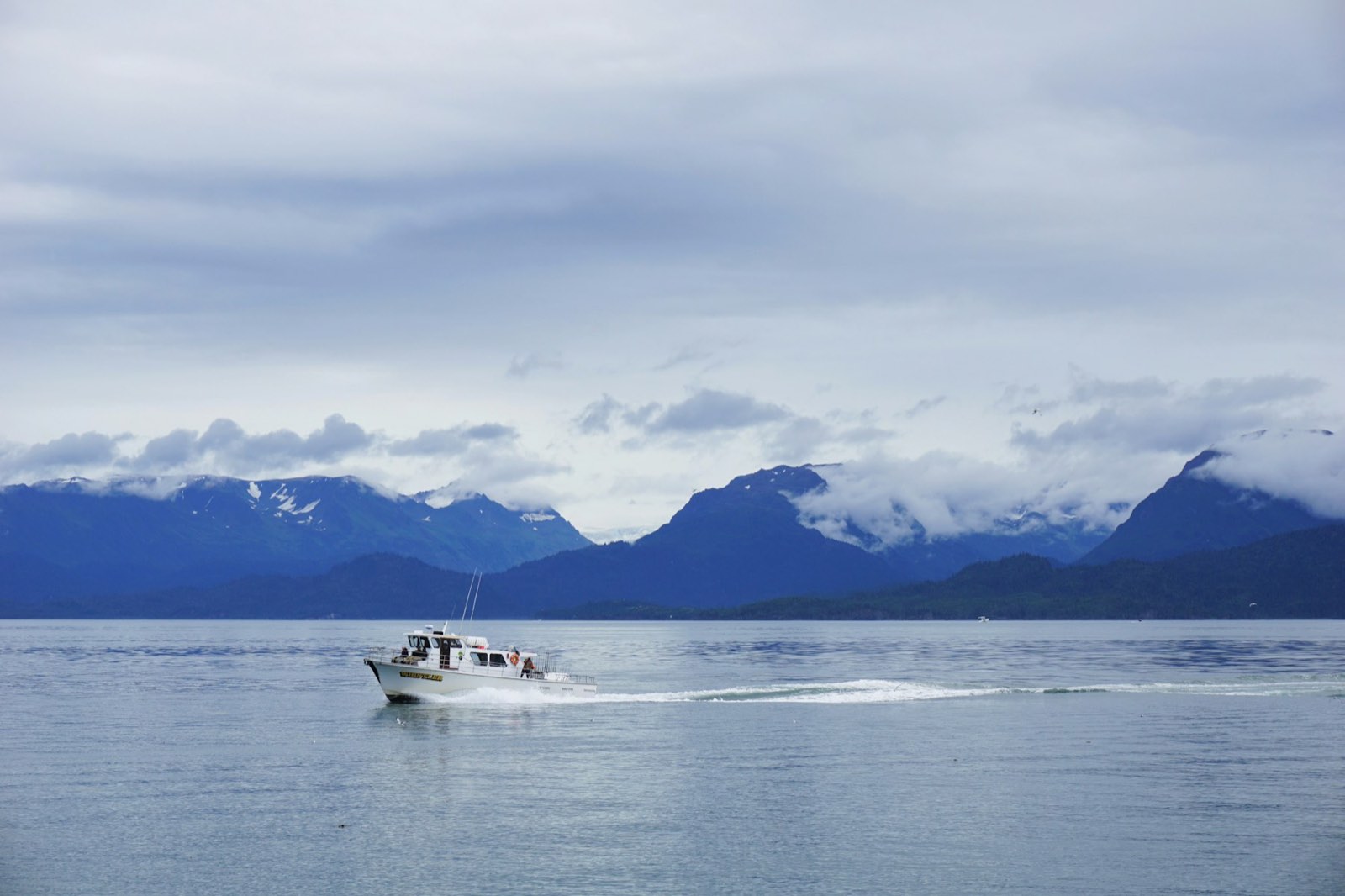 A charter boat cruising below cloud-wrapped coastal mountains