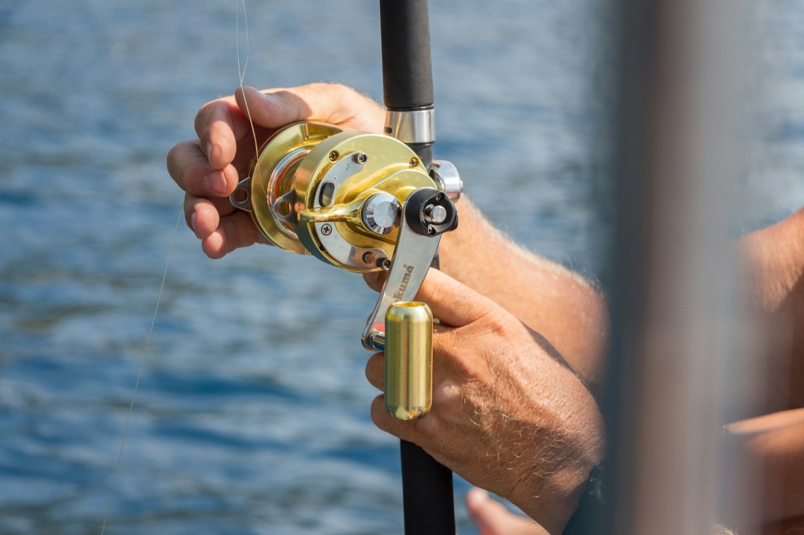A gold trolling reel in an angler's hands over blue water