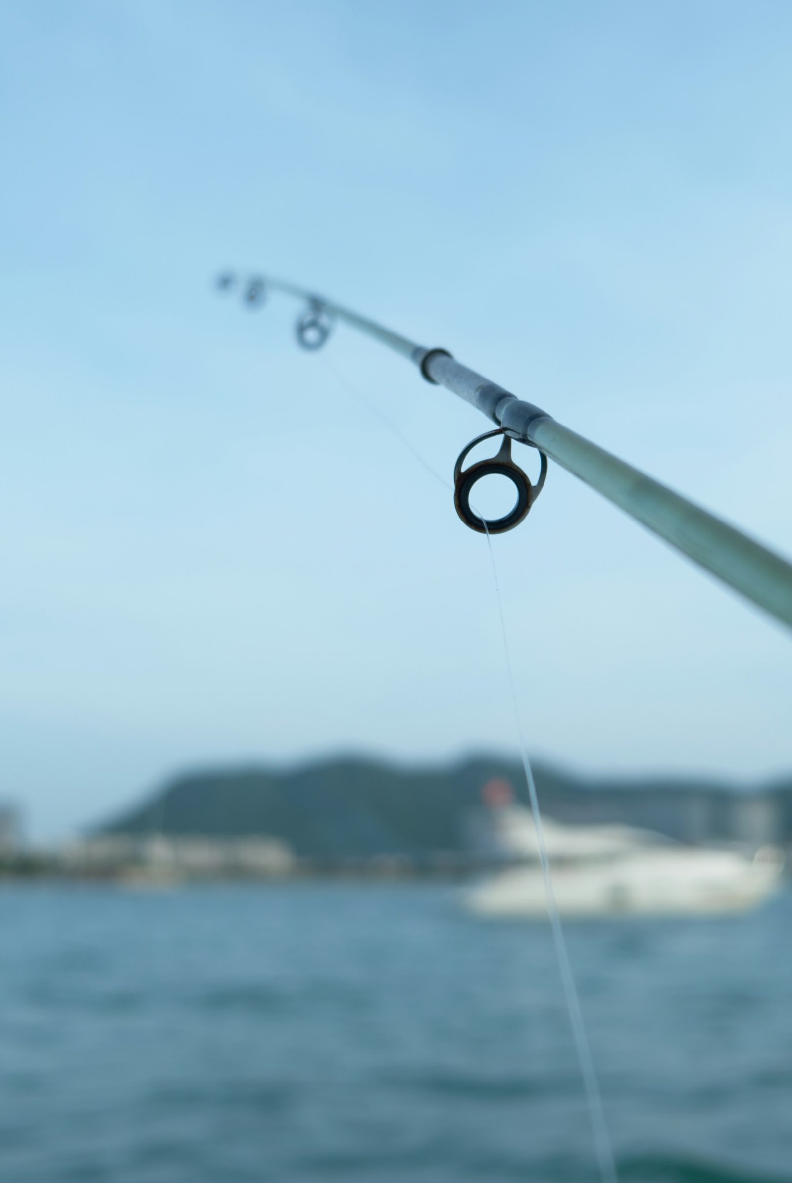 A rod tip bent over calm blue water